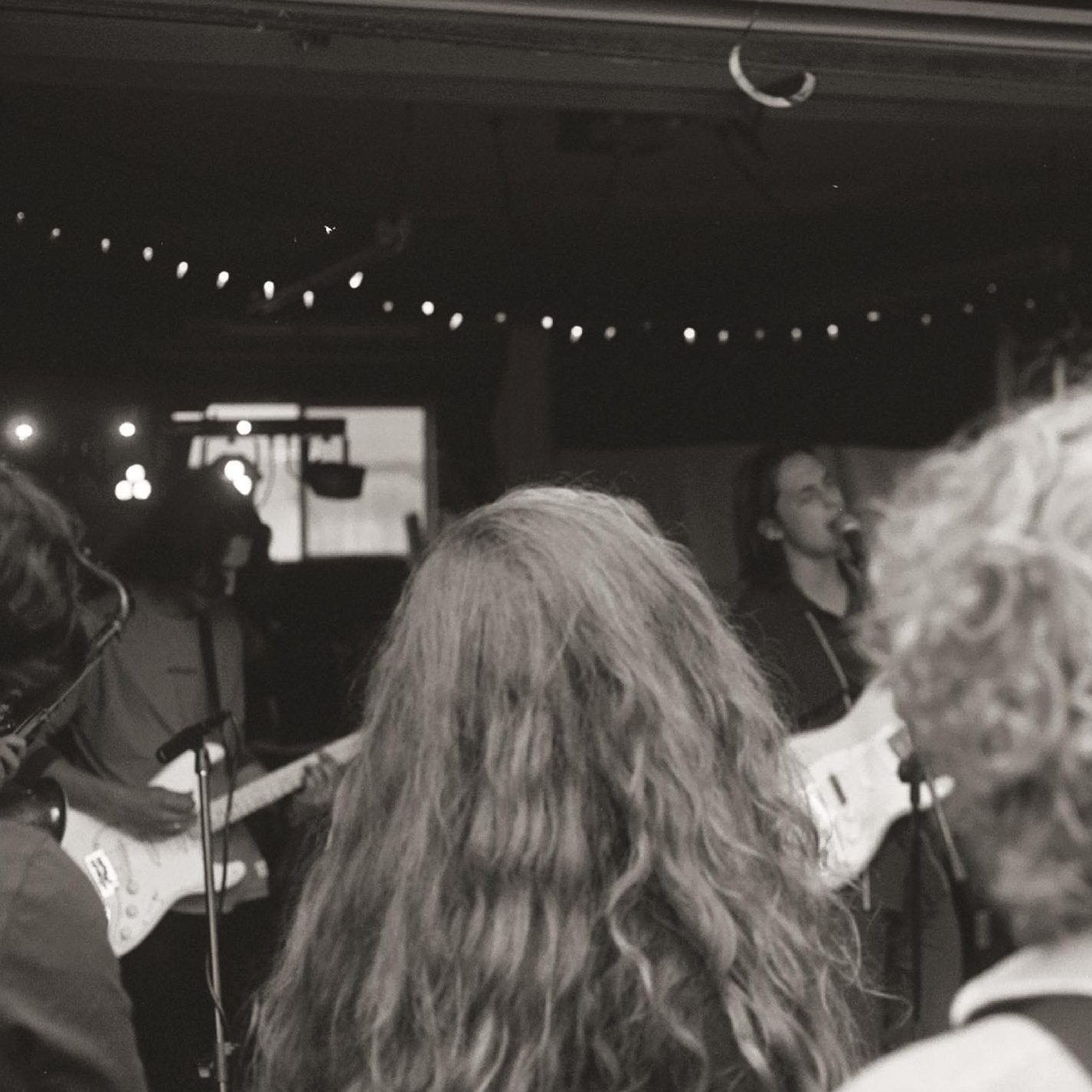 Band playing in a dim venue seen from the crowd, black and white