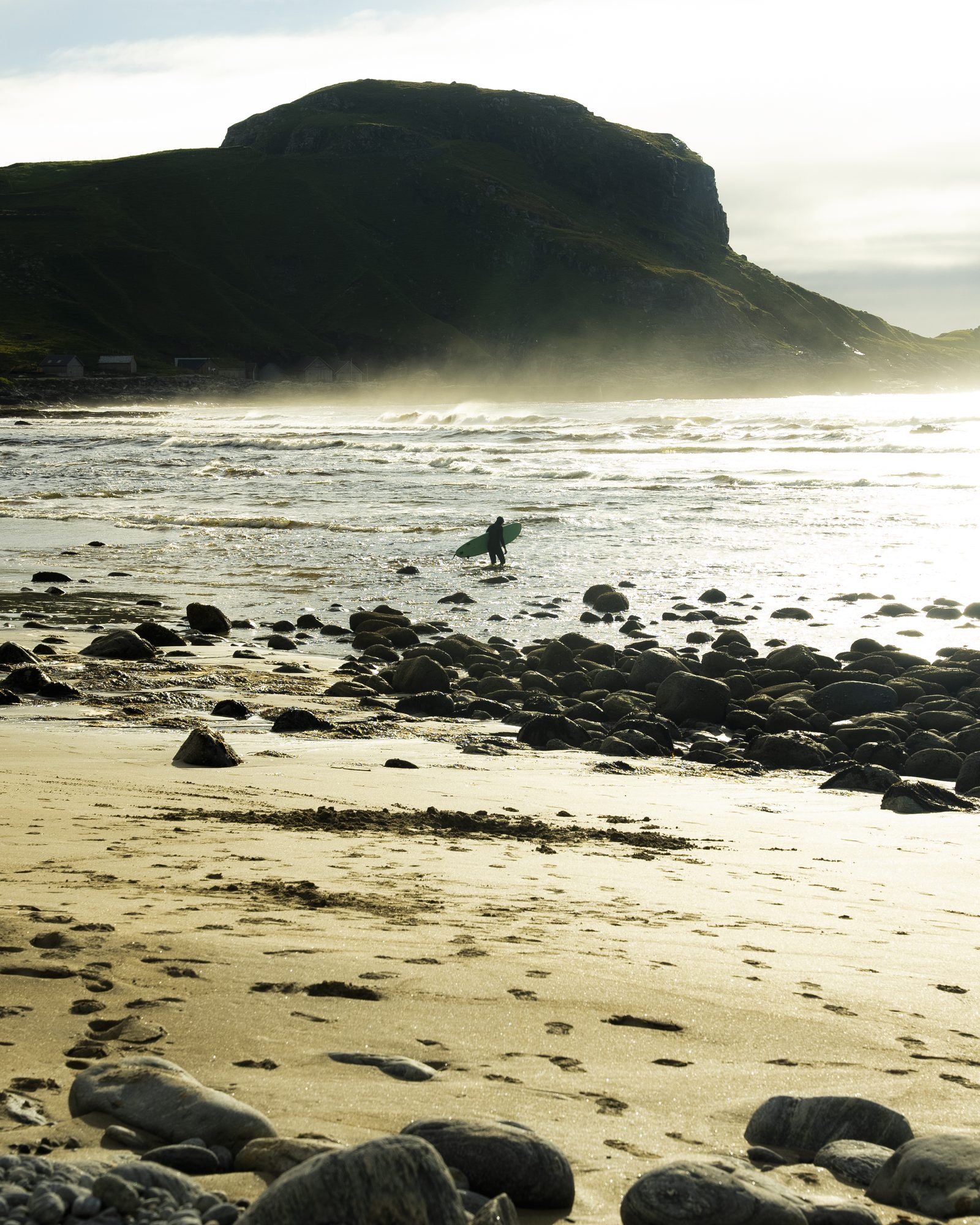 Surfer wading out at a rocky beach in mist