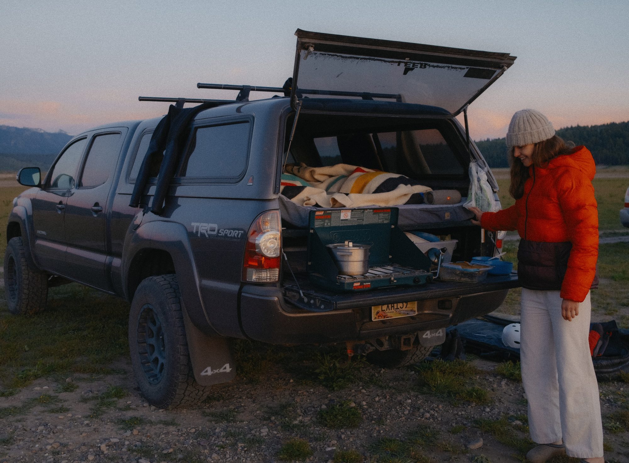 Woman cooking at the open back of a Tacoma at dusk