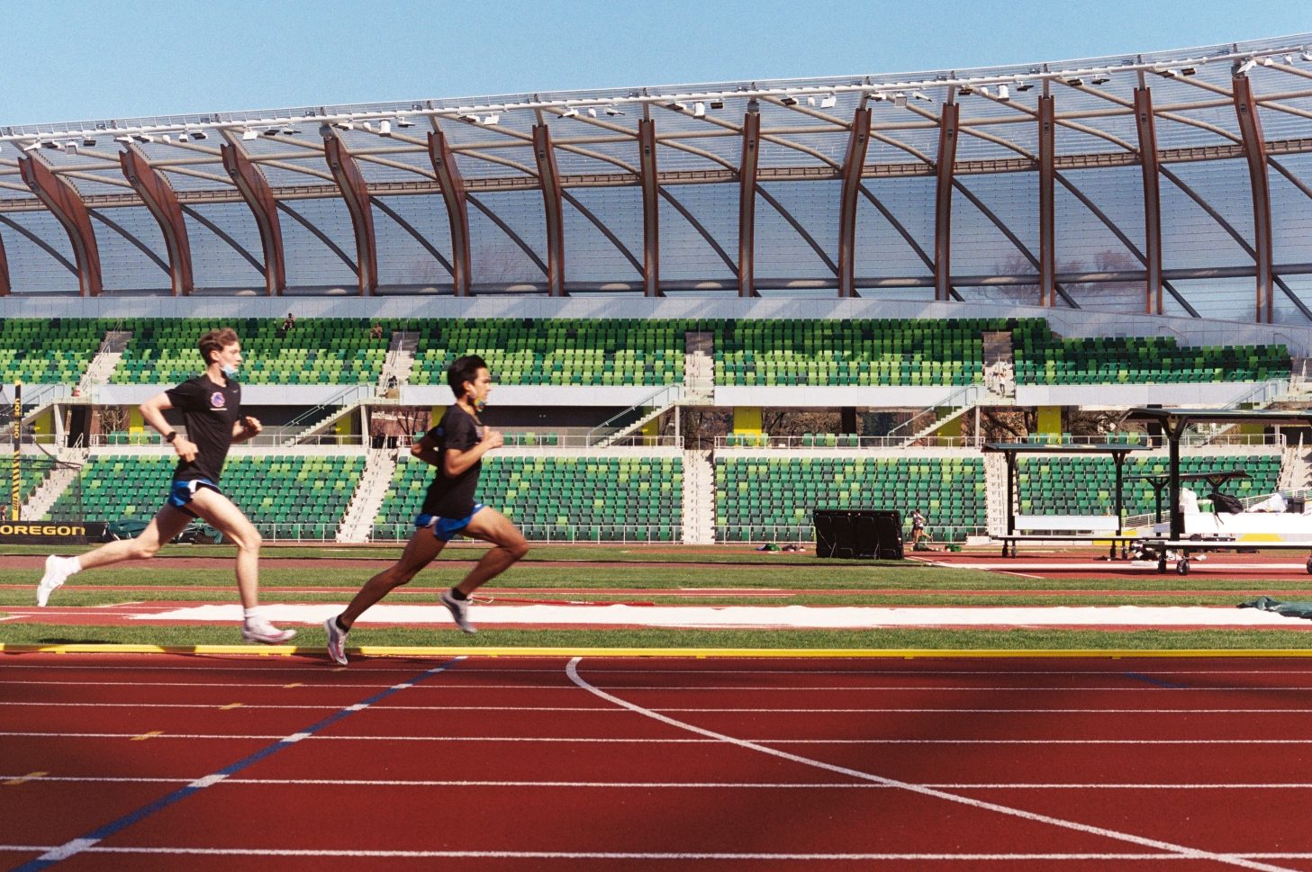 Two runners on a track in a wooden-roofed stadium