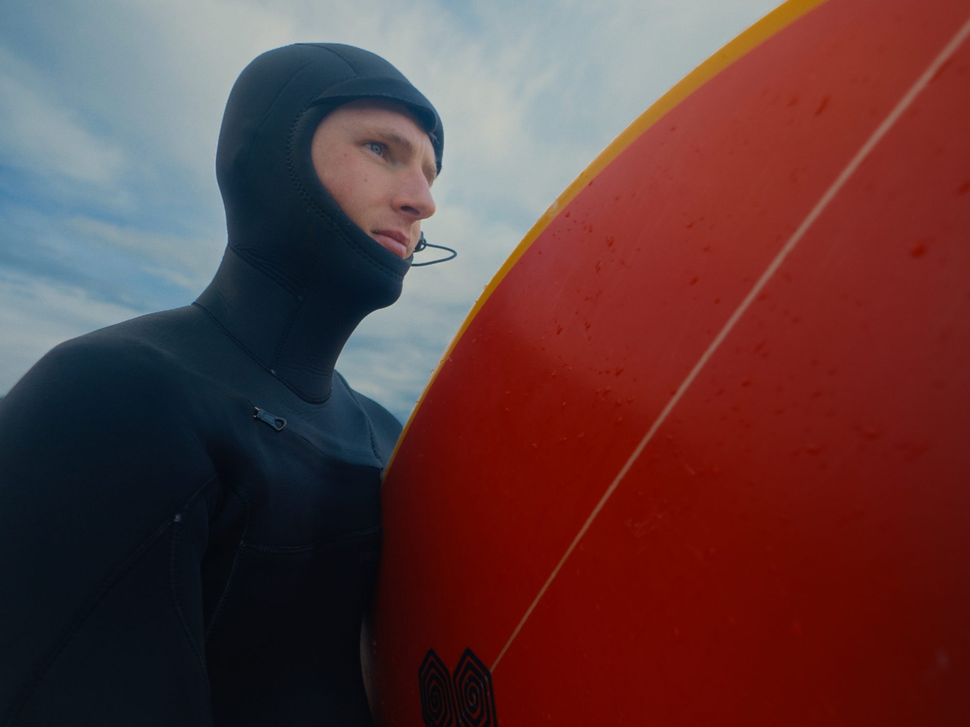 Hooded surfer beside a red board