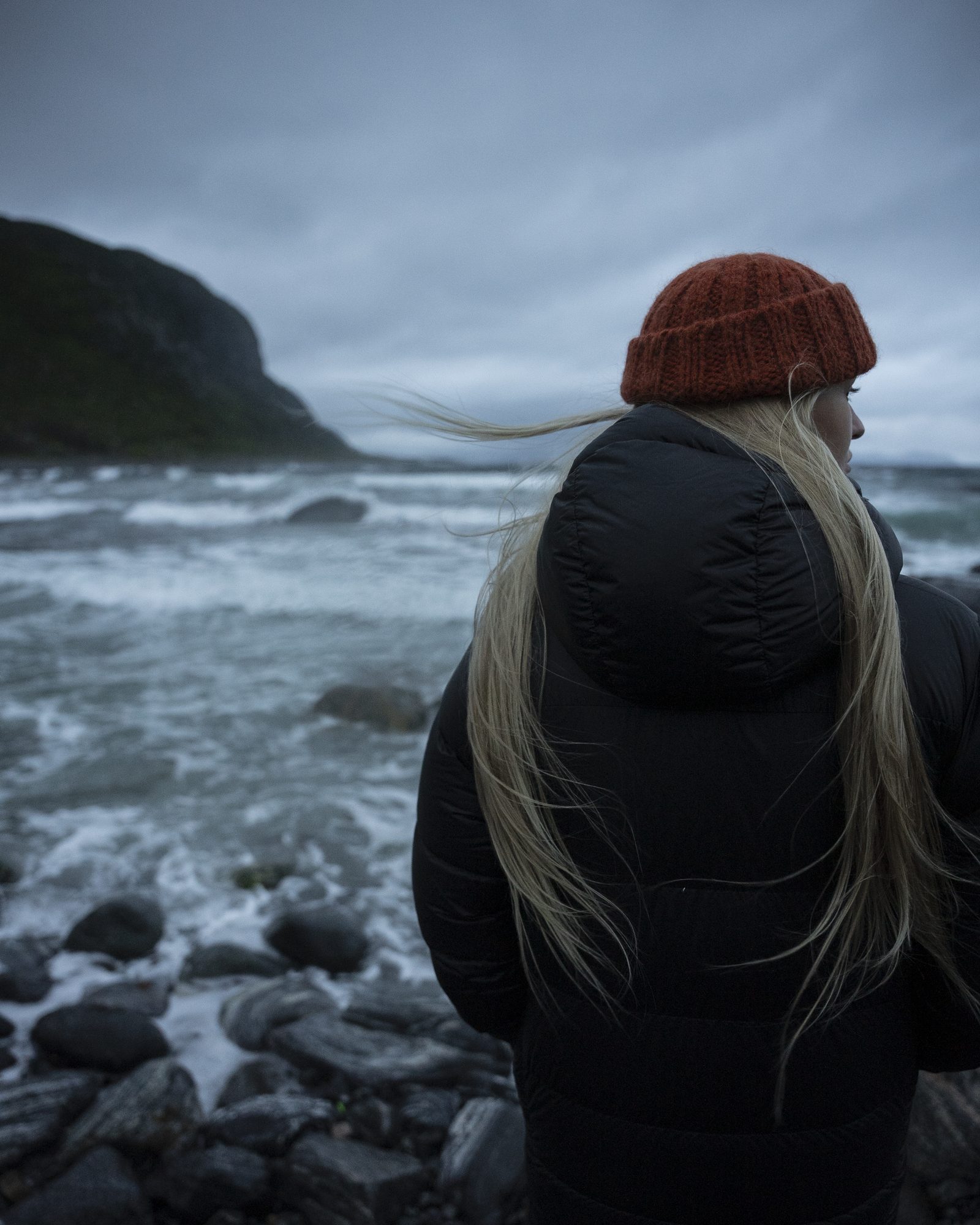 Woman in an orange beanie looking at a stormy shoreline