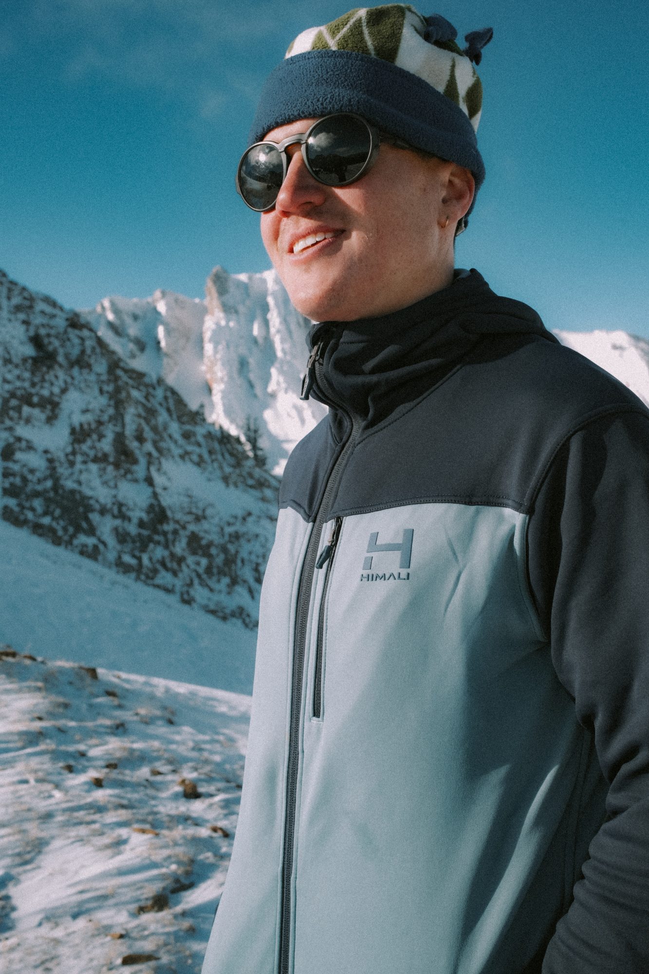 Smiling man in a blue fleece below a snowy ridge