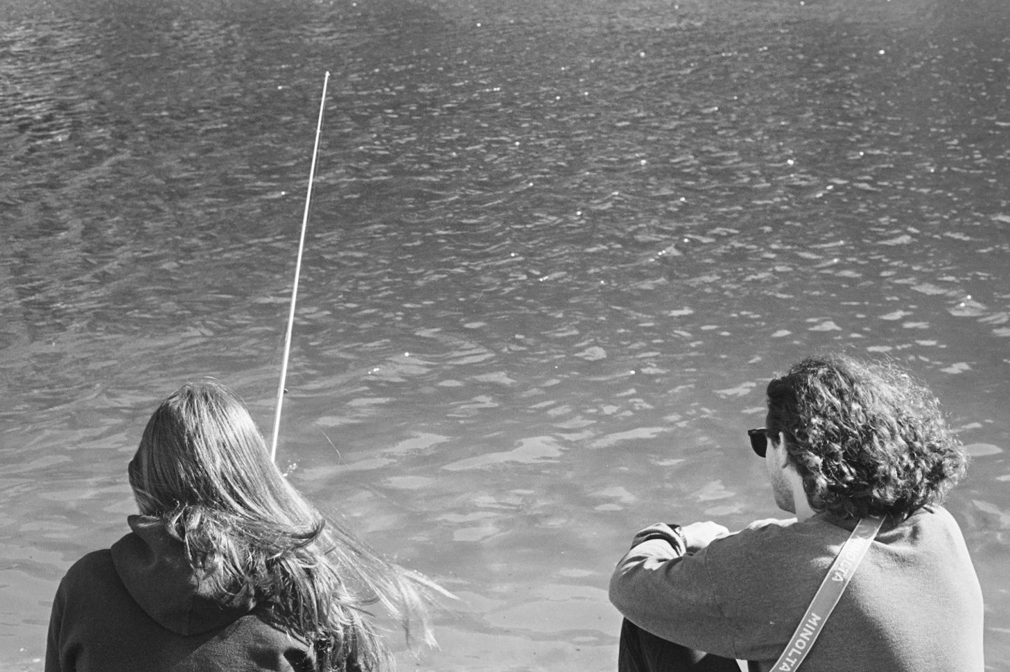 Two people fishing from a shoreline, black and white